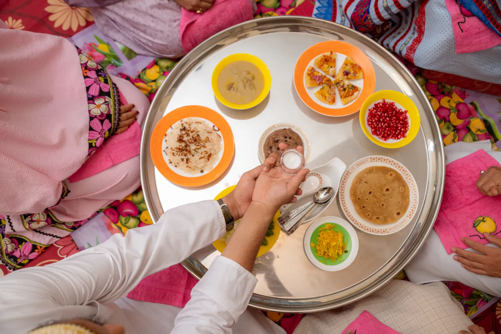 Dawoodi Bohra thaal set with small bowls of soup, samosas, pomegranate and sweets, with hands reaching in